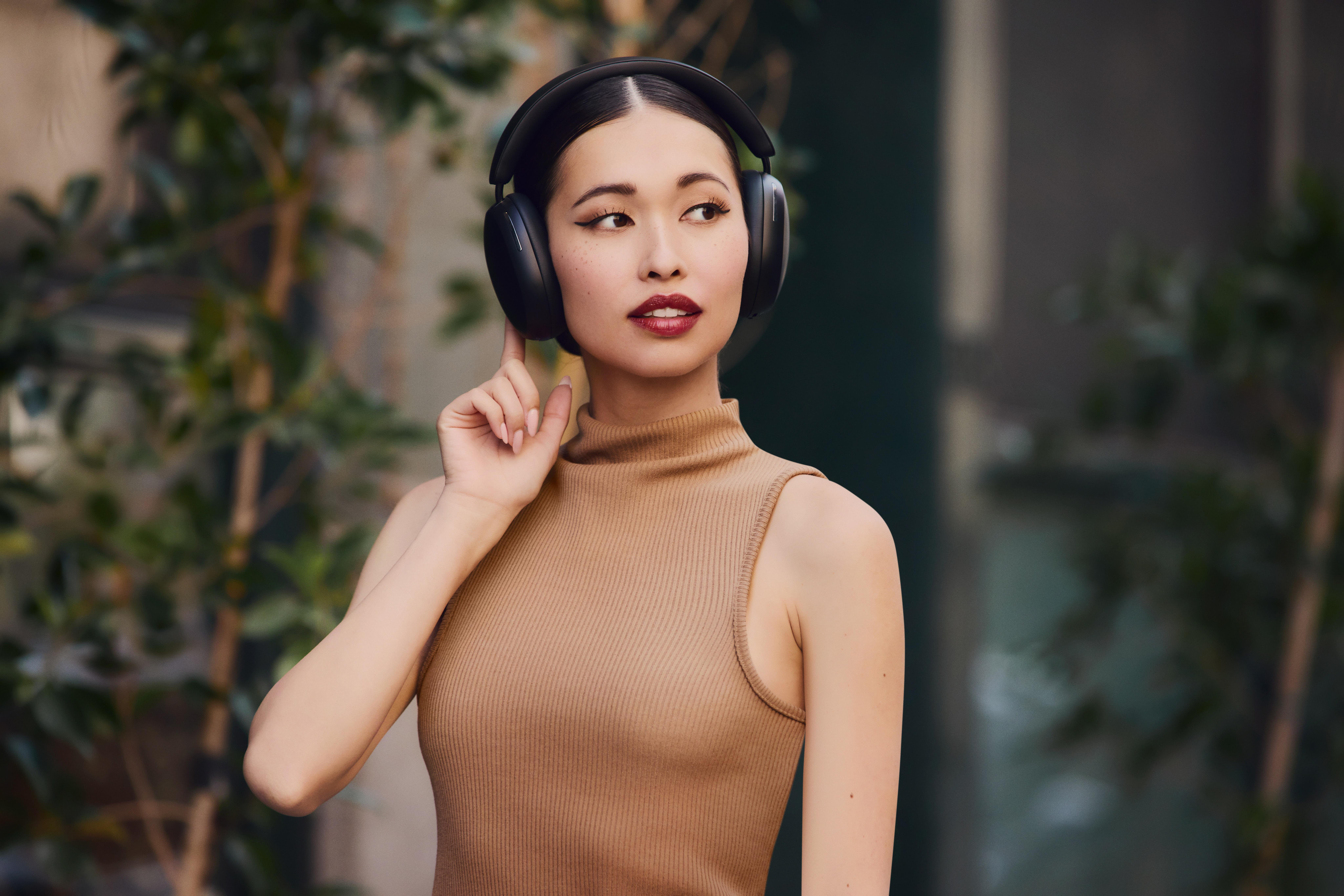 Eine Frau mit schwarzen Kopfhörern blickt nach rechts. Sie ist draußen, mit Grün im Hintergrund.
