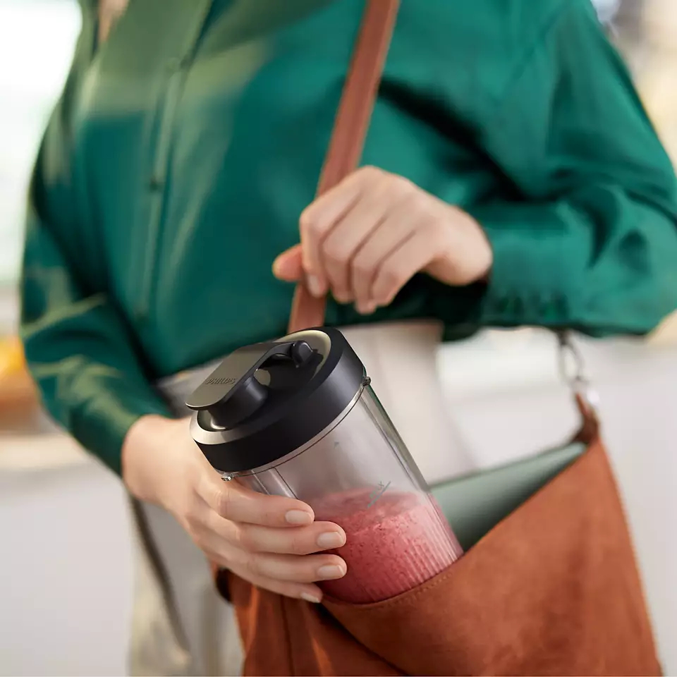 Osoba trzymająca kubek blendera z różowym smoothie, w brązowej torbie.