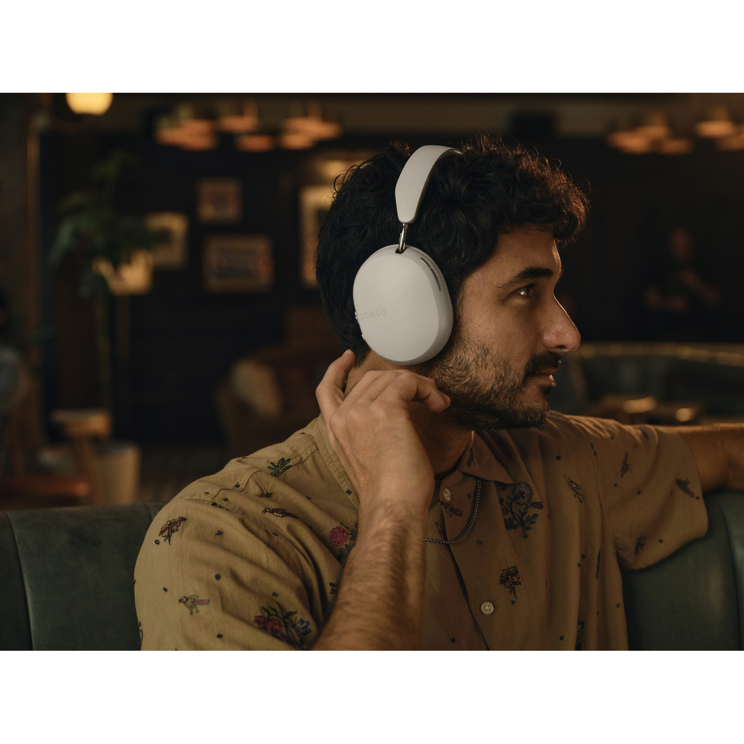A man wearing white headphones looking to the right, in a cafe.