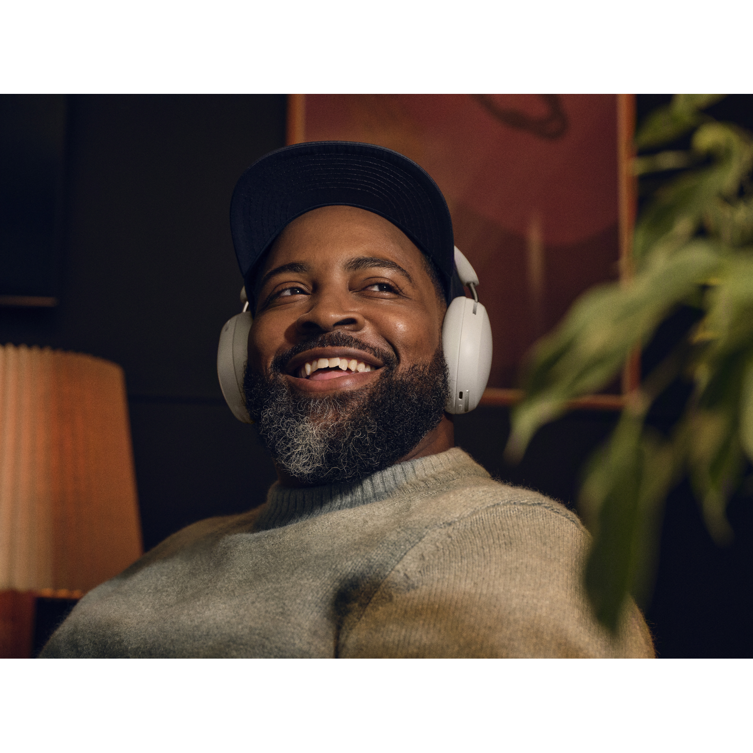 Smiling black man wearing headphones and a baseball cap, looking up.