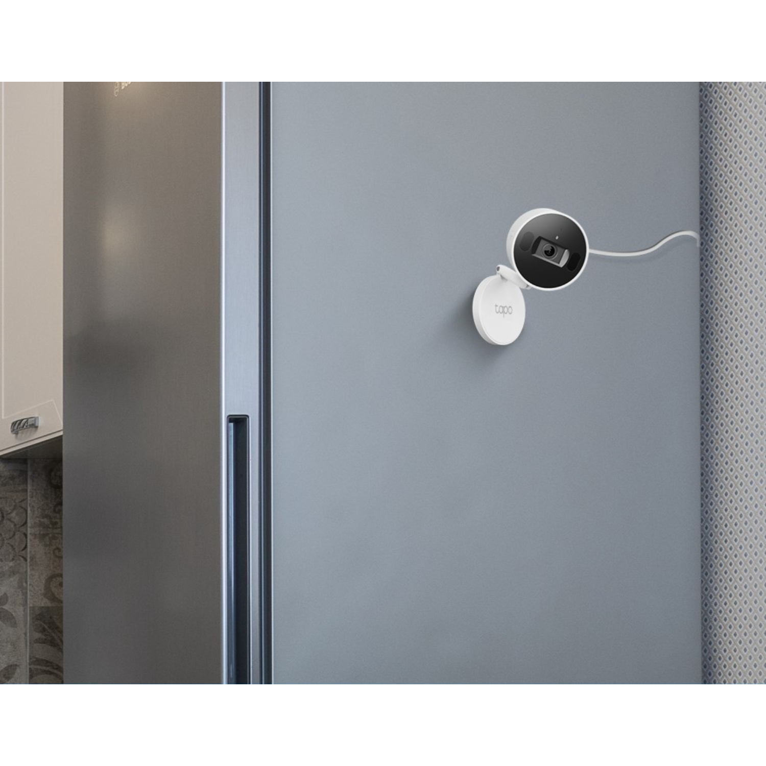 White security camera mounted on a gray wall. A white refrigerator is on the left.
