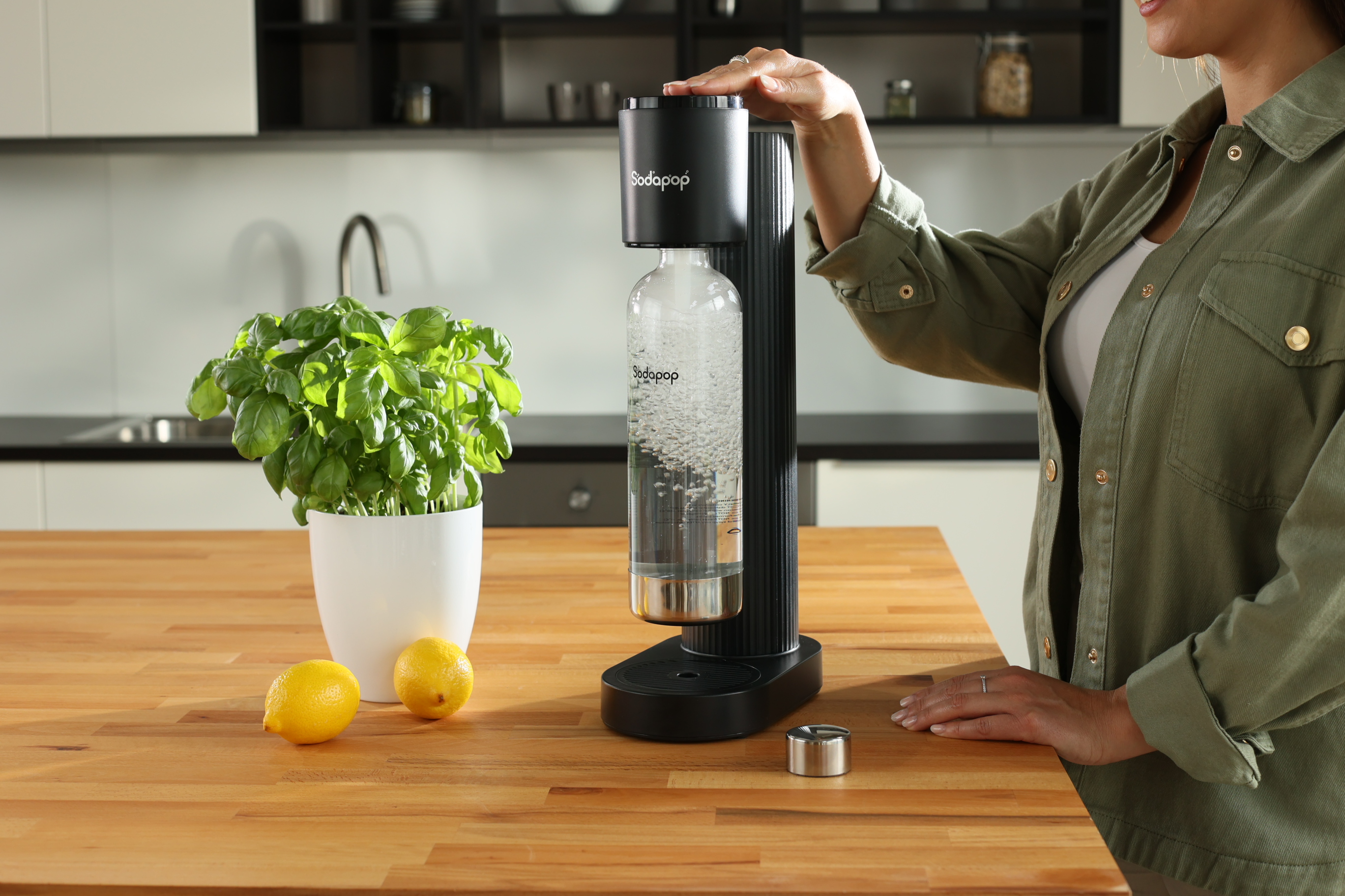 Eine Frau benutzt einen SodaStream auf einer Holztheke mit Zitronen und einer Pflanze.