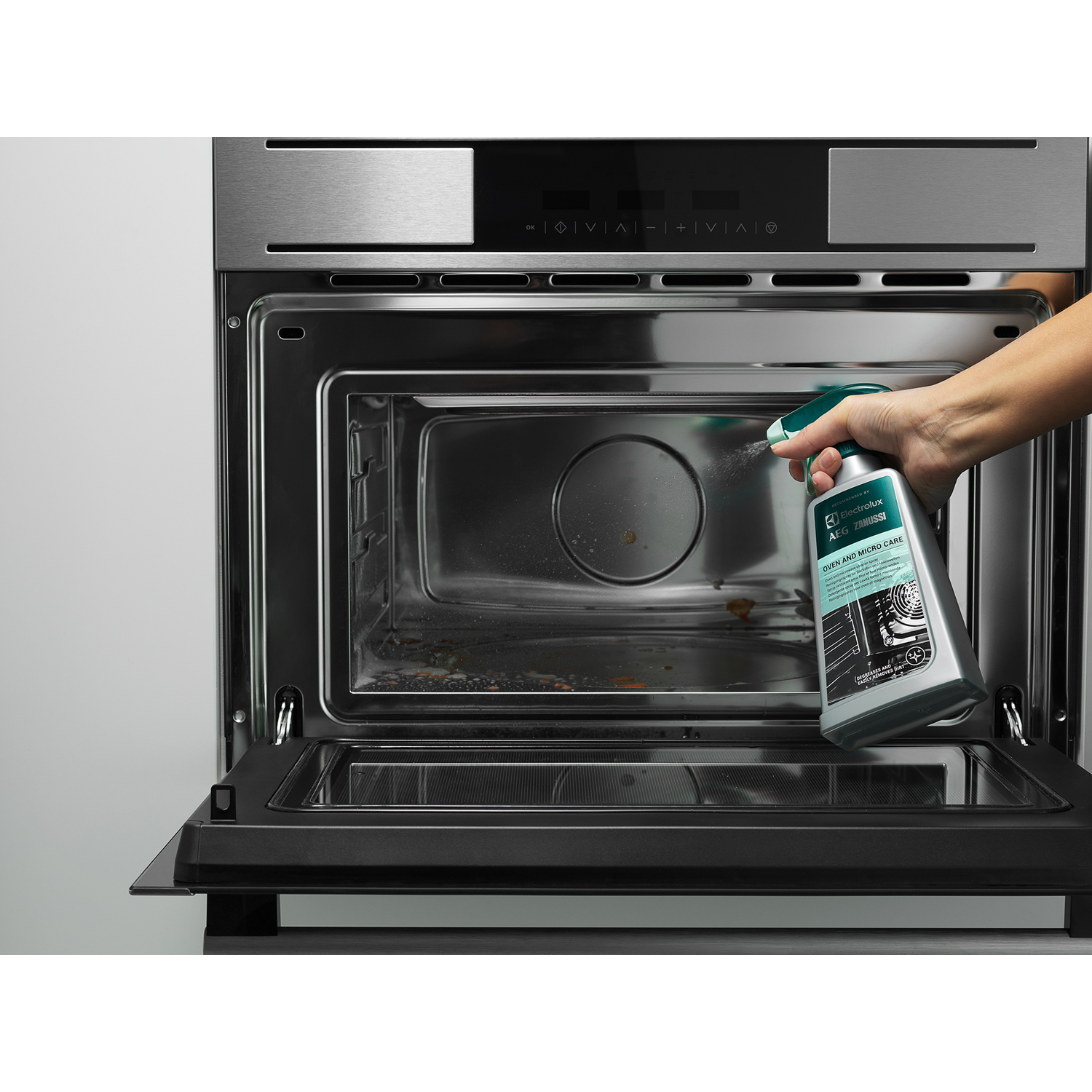 Una persona spruzza un detergente per forno all'interno di un forno aperto.