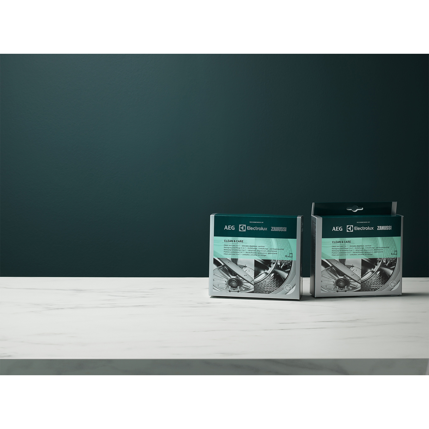 Due scatole di prodotti AEG Electrolux Zanussi su superficie bianca contro sfondo verde acqua scuro.
