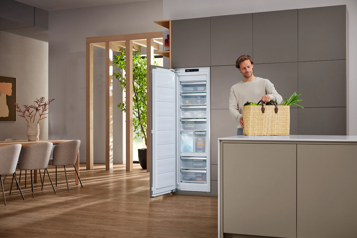 Mann steht mit Lebensmitteln am Kühlschrank. Im Hintergrund ein Essbereich.