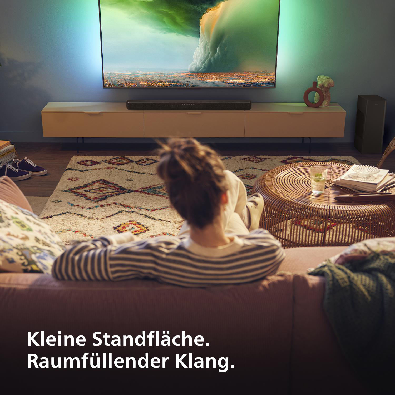 Person auf Couch sieht fern, mit Soundbar und Teppich im Wohnzimmer.