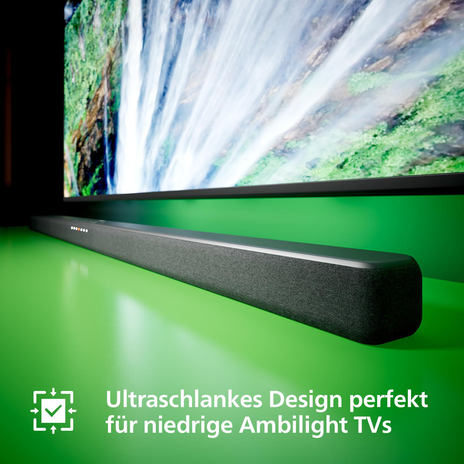 Eine Soundbar auf einem grünen Tisch mit einem Fernseher im Hintergrund, mit Text auf Deutsch. Der Fernseher ist dahinter.