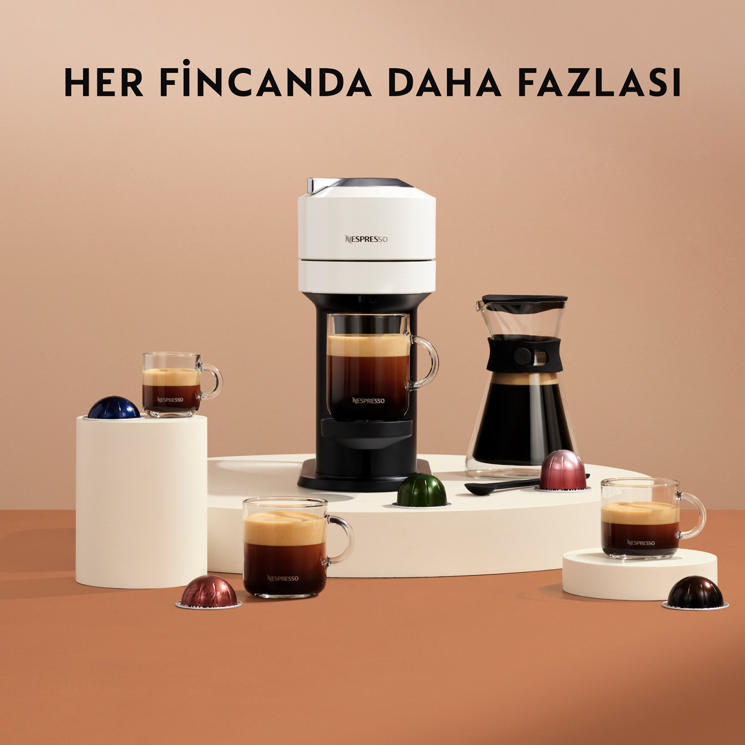 Beyaz bir Nespresso kahve makinesi, fincanlar ve kapsüllerle. Metin: 'HER FINCANDA DAHA FAZLASI'.