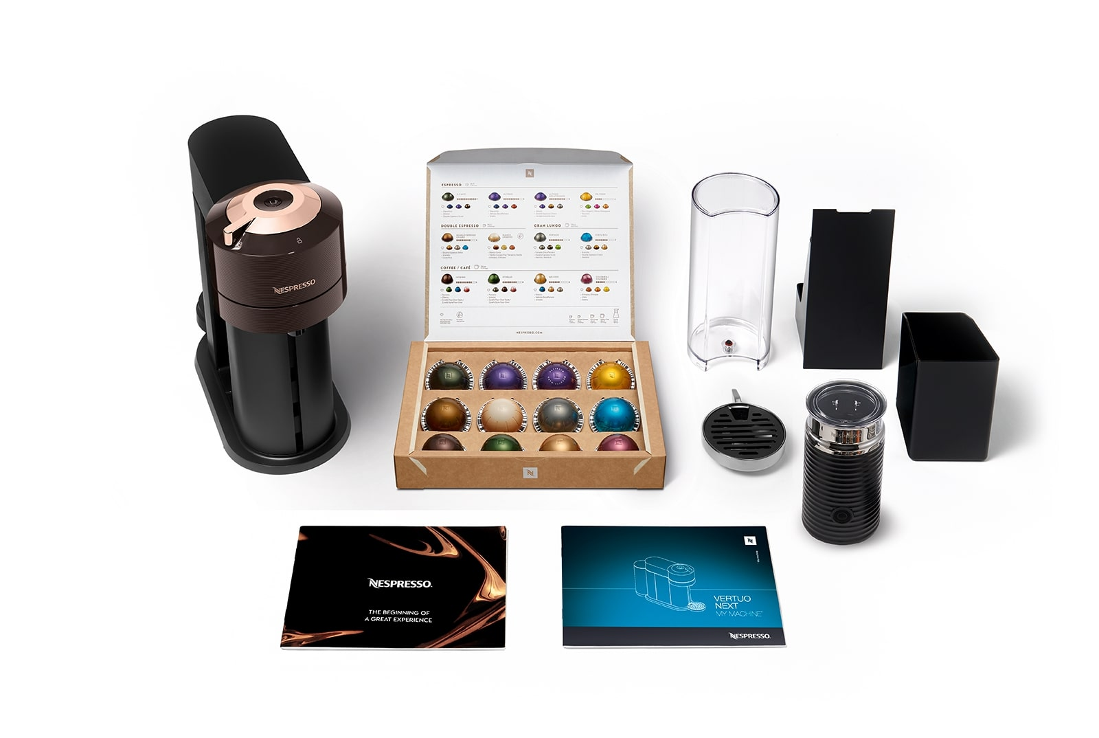 Nespresso Vertuo Next kahve makinesi, kapsüller, süt köpürtücü ve aksesuarlar beyaz bir yüzeyde.