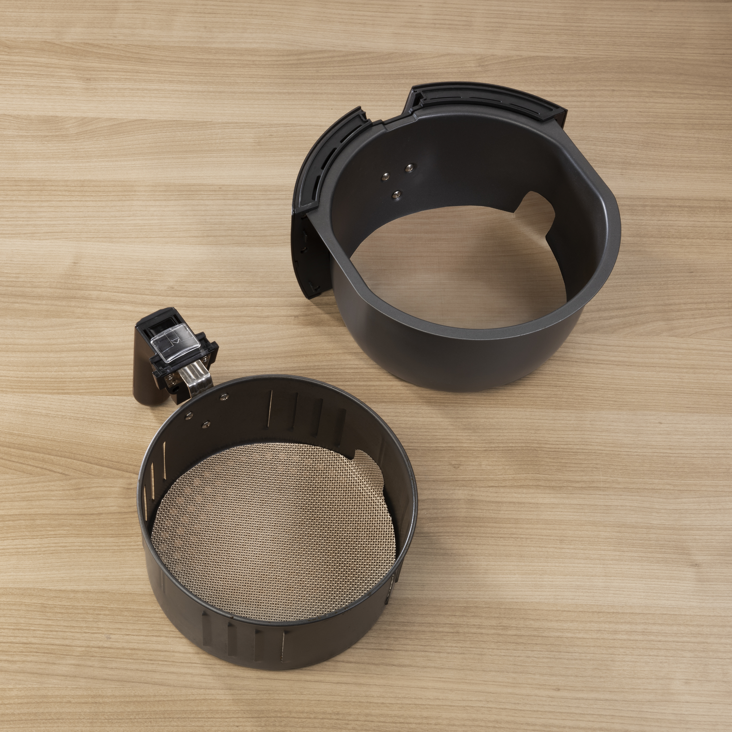Air fryer components, including a basket and a detached top part, on a wooden surface.