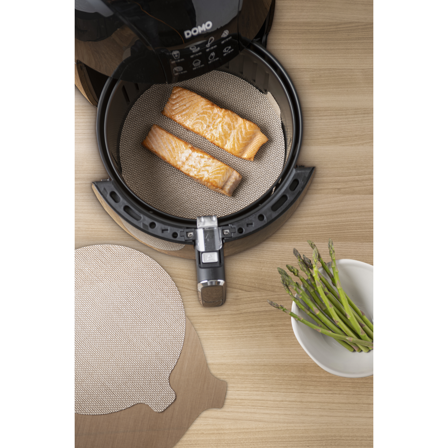 Air fryer with salmon and asparagus on a wooden surface.