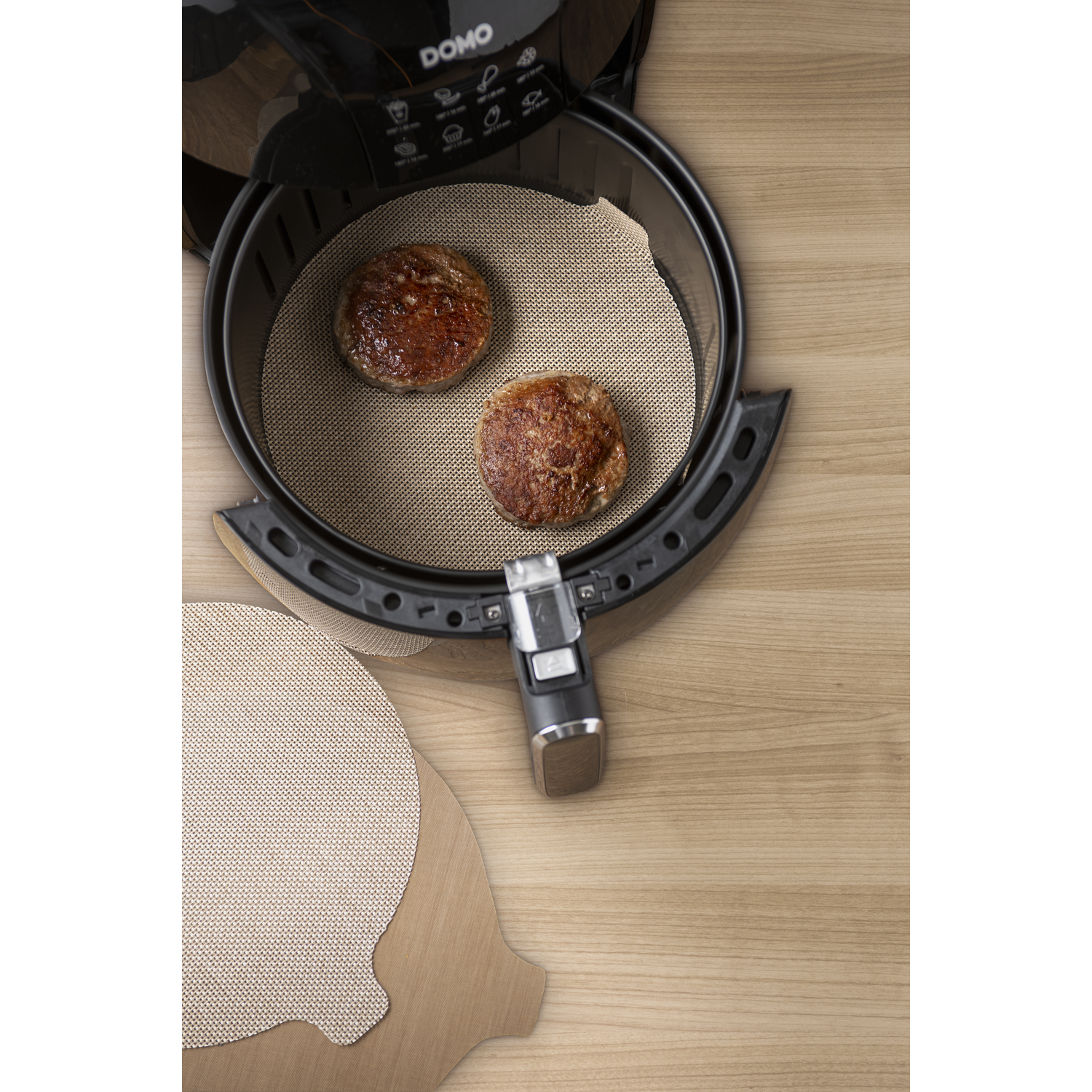 Inside an air fryer, two cooked patties sit on a textured tray. Beside it, an extra tray.