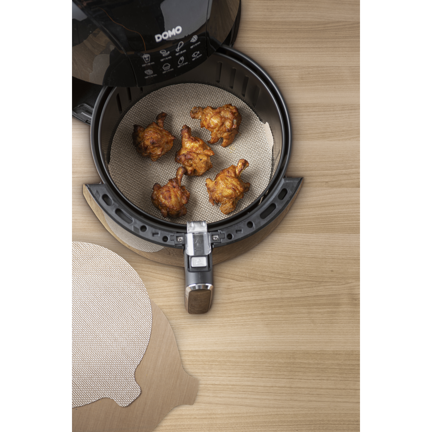 An air fryer with cooked chicken pieces inside, with a parchment paper. Wooden surface background.