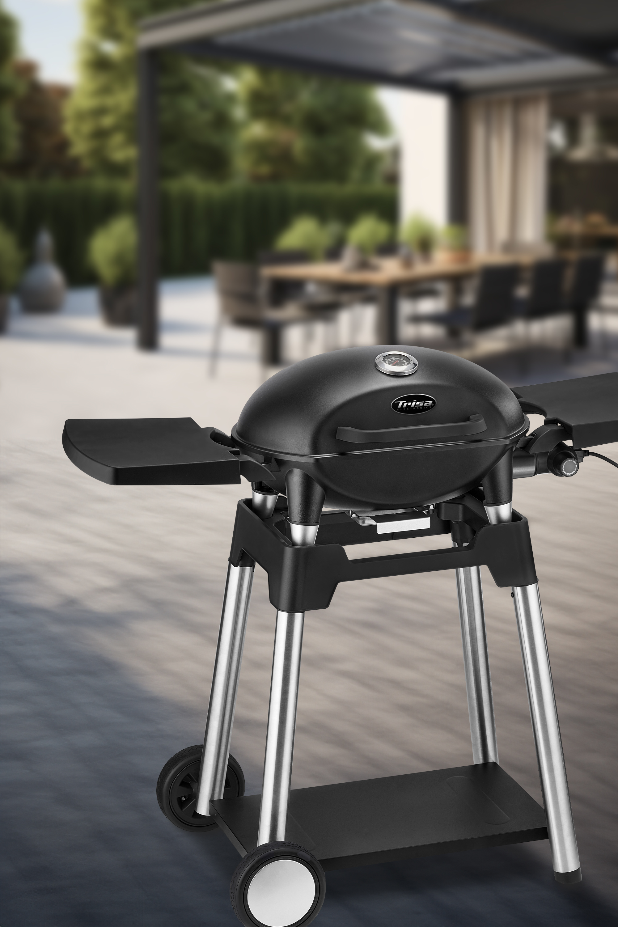Ein schwarzer Grill auf einem rollbaren Ständer, auf einer Terrasse mit verschwommenem Sitzbereich im Hintergrund.