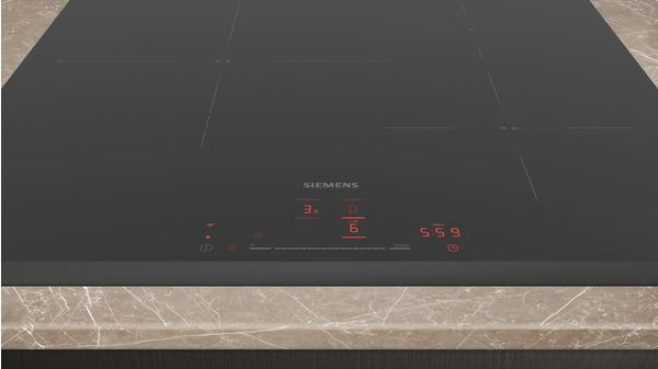 Placa de inducción negra con pantalla roja. Características de la marca y ajustes de cocción. Superficie de mármol marrón claro.