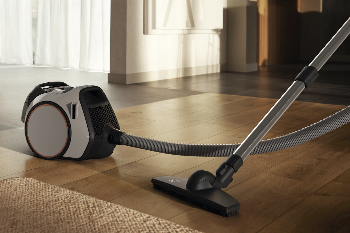 Aspirateur sur plancher en bois, avec un tapis beige au premier plan.