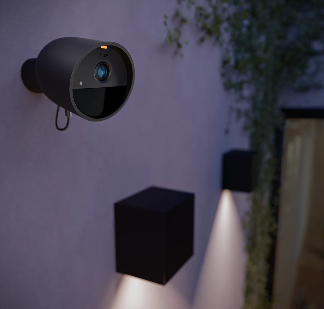 Czarna kamera bezpieczeństwa na ścianie, obok czarnej lampy w kształcie kostki.