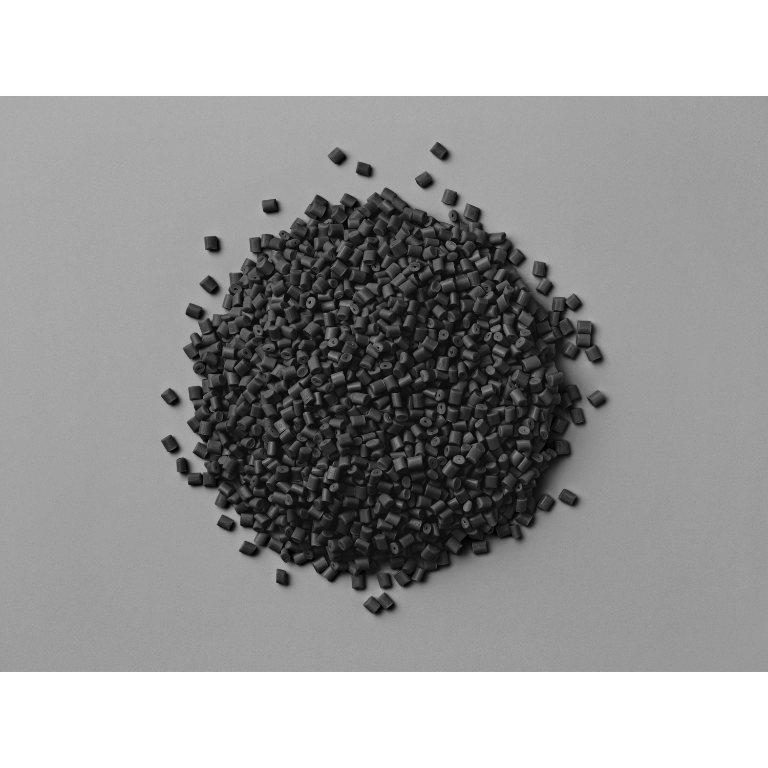 Tas de granulés de plastique noir sur une surface grise. Petites formes uniformes.