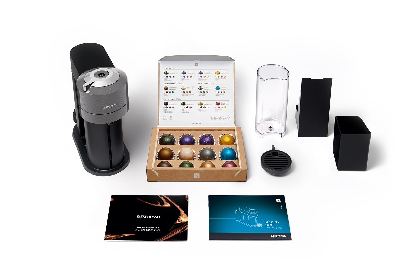 Beyaz bir yüzey üzerinde aksesuarları ve bir kutu kapsülle bir Nespresso makinesi.