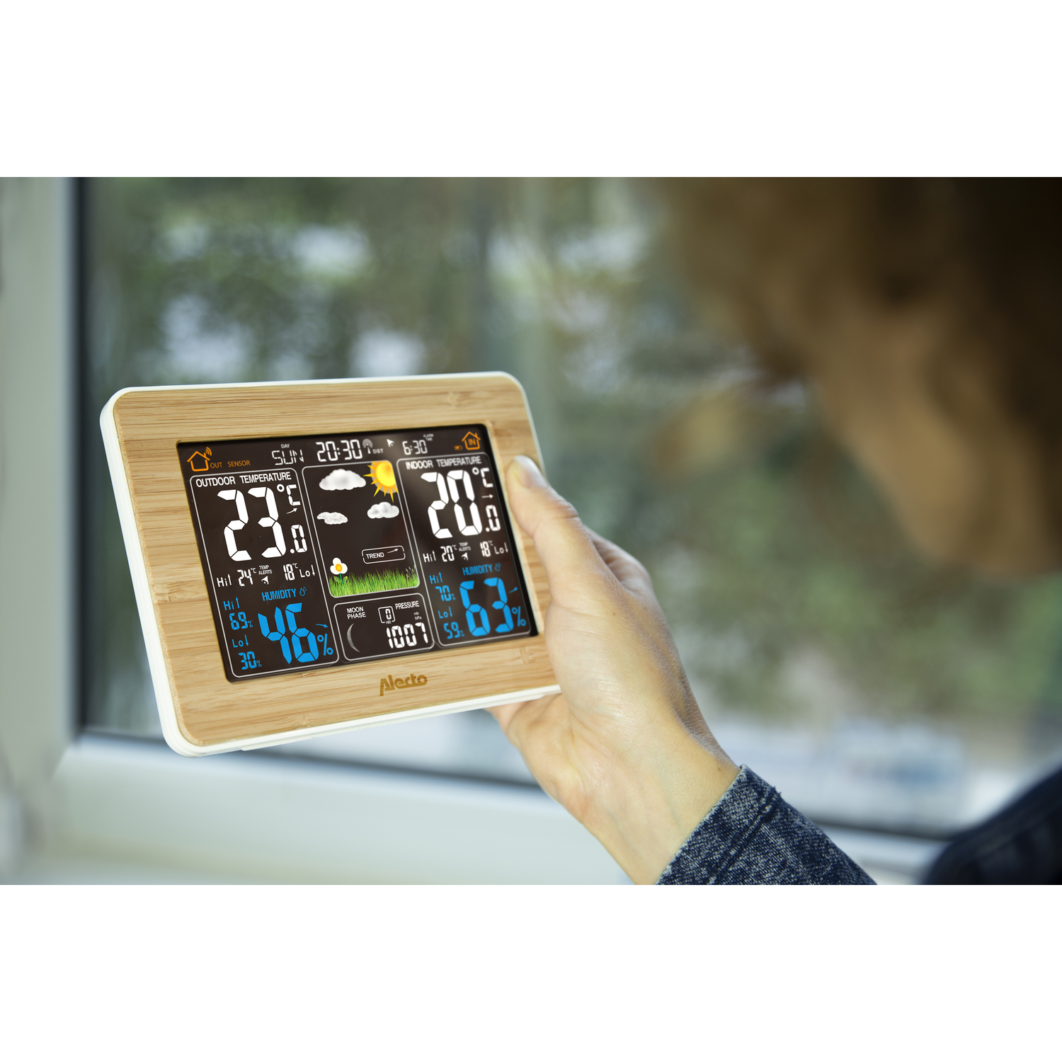 A woman holding a weather station. The station displays temperature, humidity, and weather icons.