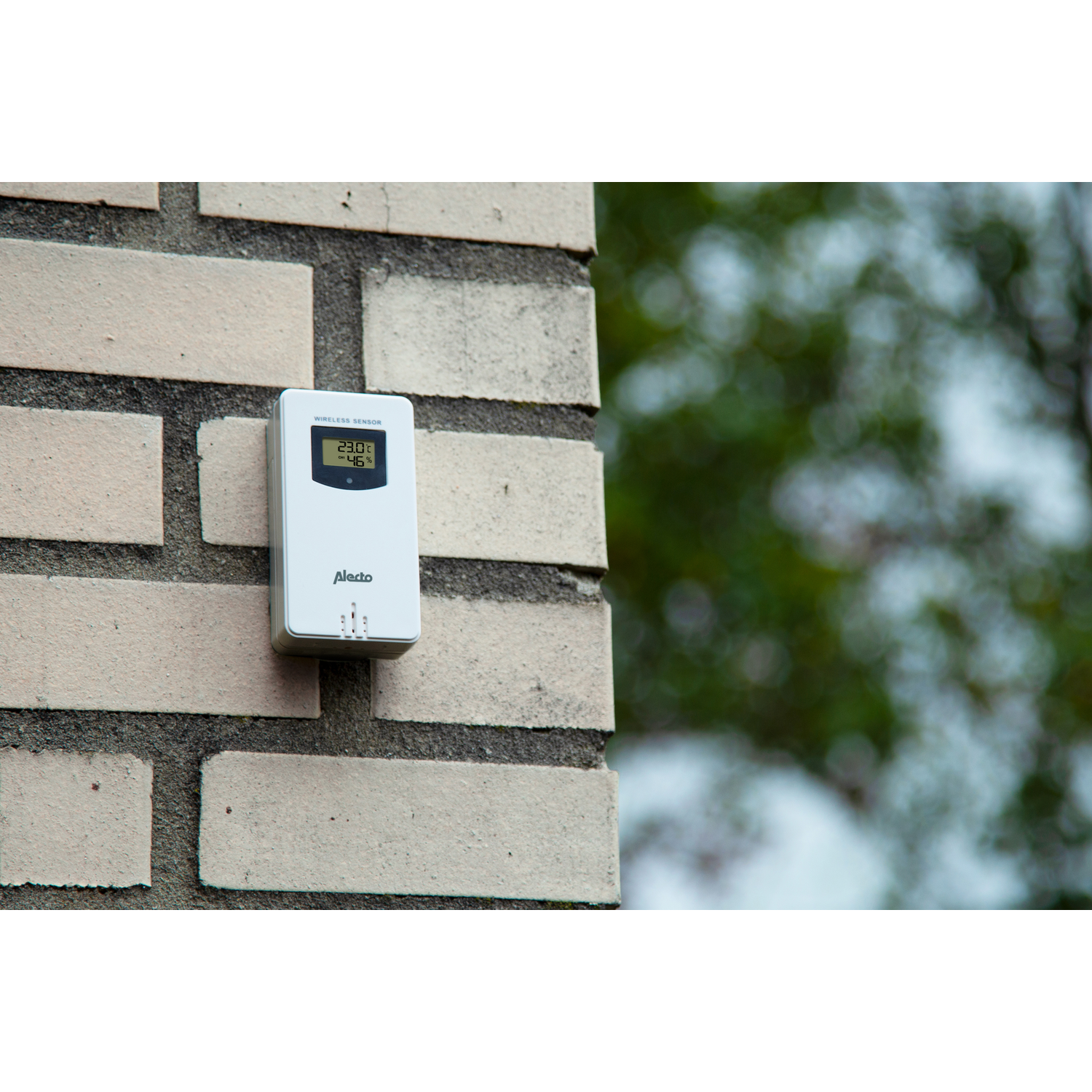 White weather sensor mounted on a brick wall. Displays temperature and humidity.