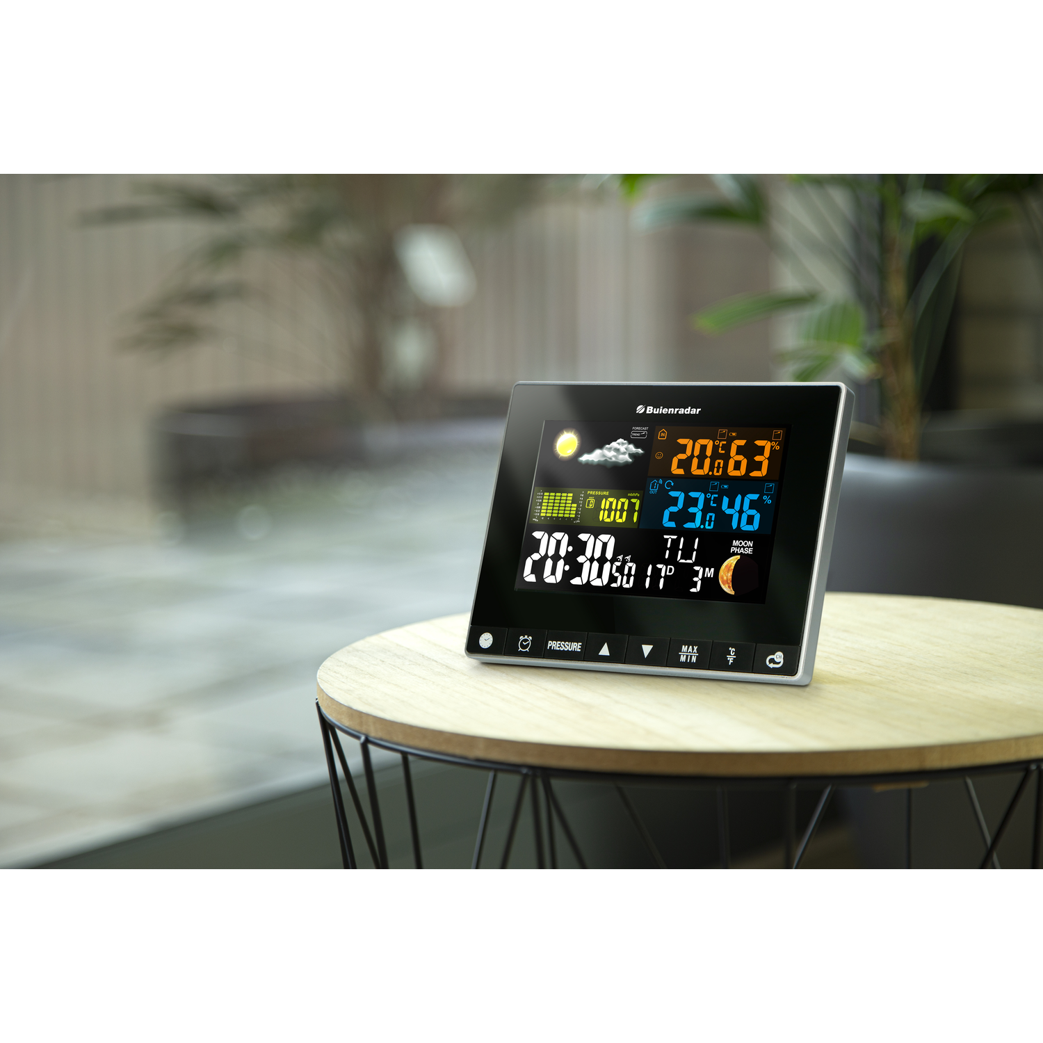 A weather station displays time, temperature, and weather conditions on a table.