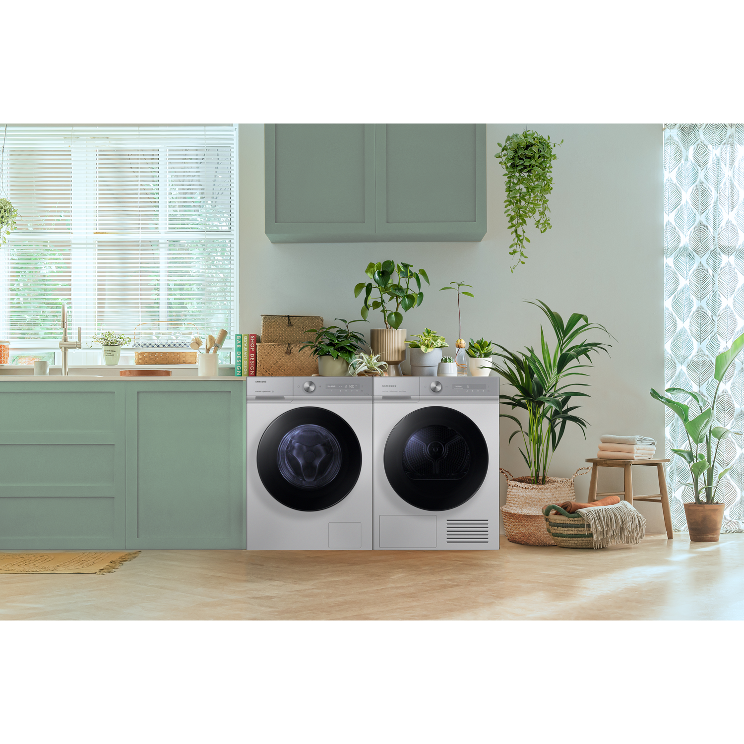 Two silver washing machines with black doors in a room with plants and a window.