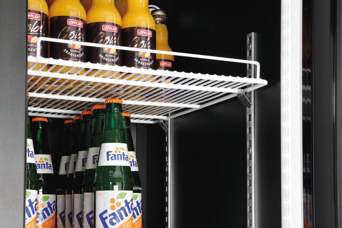 Ein Kühlschrankregal mit Orangensaft- und Fanta-Flaschen. Die Orangensaftflaschen sind beschriftet. Die Fanta-Flaschen sind grün.