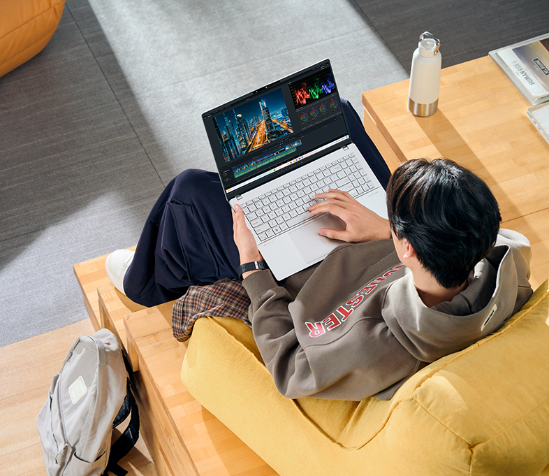 Személy laptopjával az ölében, videót szerkeszt. Egyéb tárgyak a közelben.