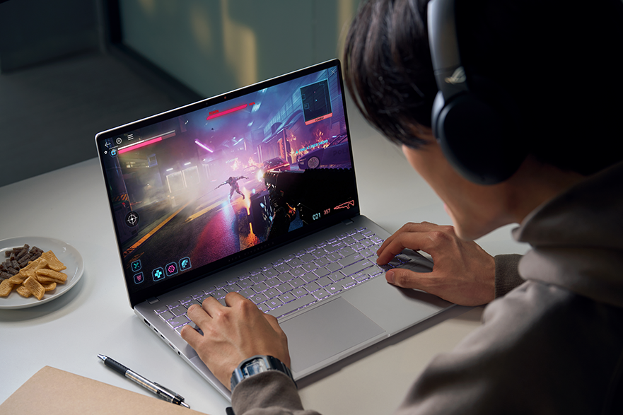 Fejhallgatós személy játékozik laptopon, világító billentyűzettel.