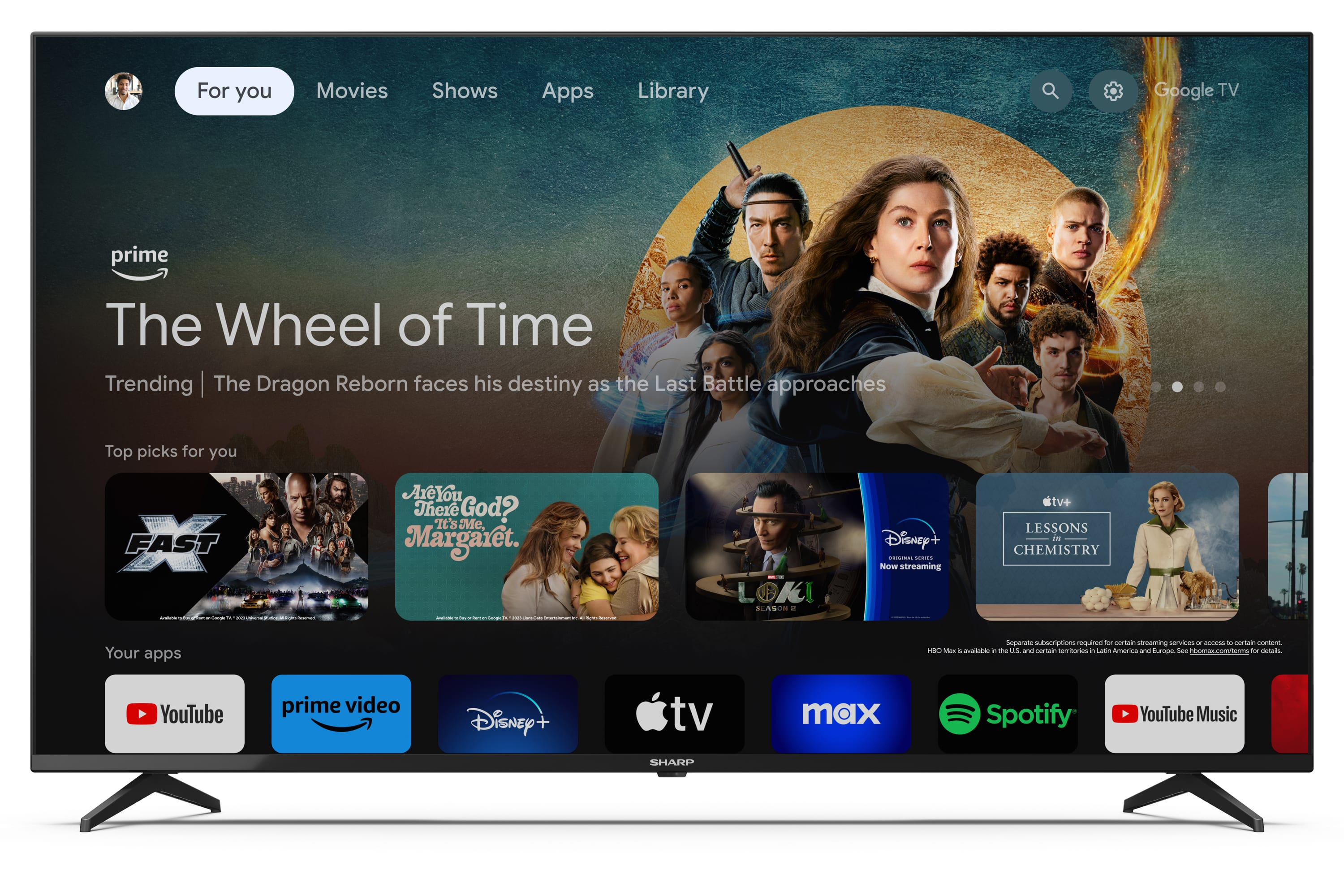 Un televisor grande muestra aplicaciones de streaming, con 'The Wheel of Time'. Marco y soporte negro.
