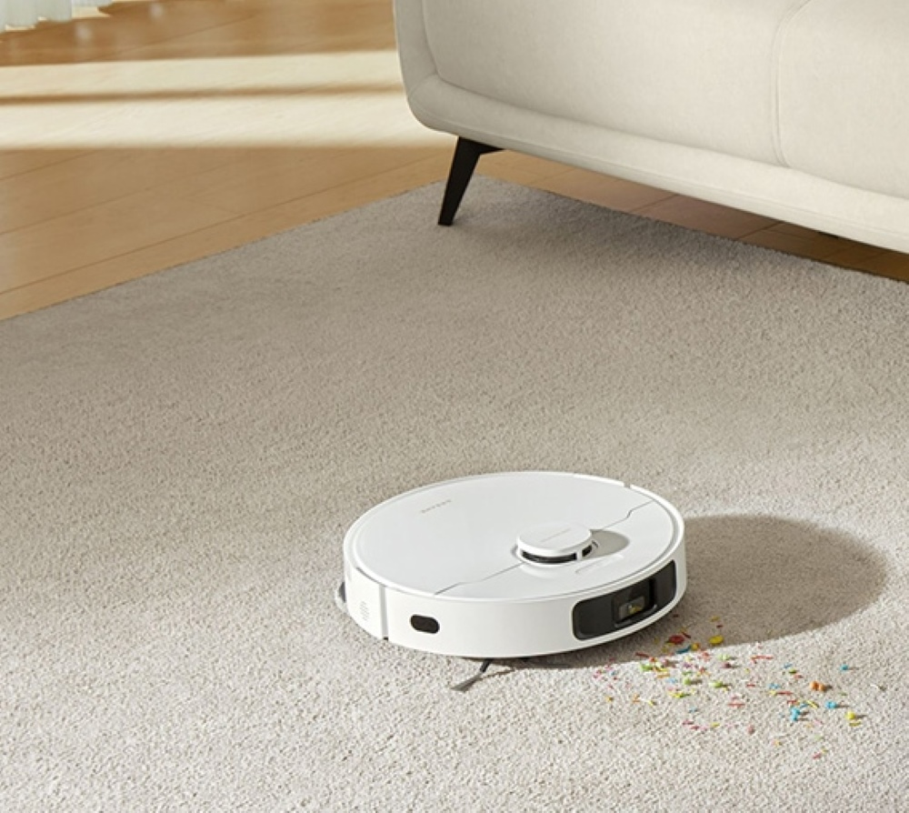 Biały odkurzacz automatyczny na dywanie z kolorowymi okruchami.