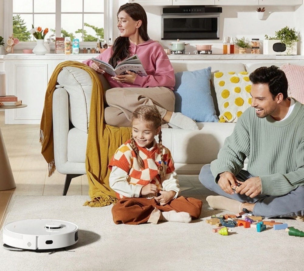 Rodzina w salonie. Robot sprzątający na podłodze. Ludzie na sofie i podłodze.