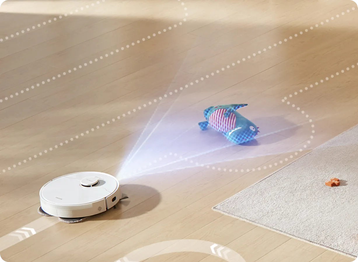 Robot sprzątający na drewnianej podłodze, zabawka ryba i mała pomarańczowa zabawka. Biały dywan w tle.