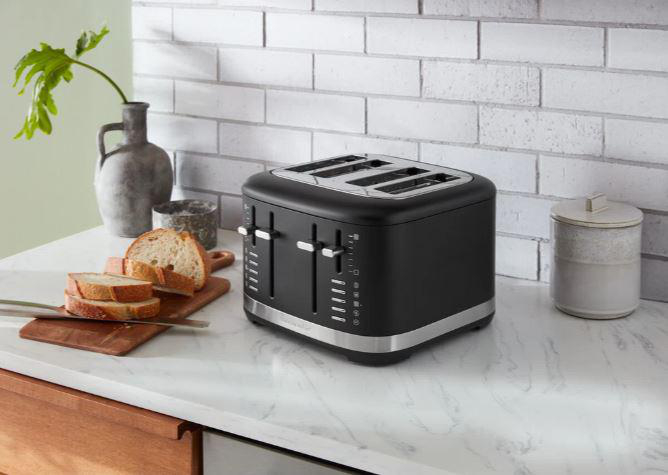 Ein schwarzer Toaster mit vier Schlitzen, Brotscheiben und einem Schneidebrett auf der Arbeitsplatte.