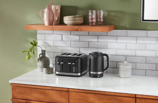 Schwarzer Toaster, Wasserkocher und Zubehör auf einer Arbeitsplatte mit weißem Backstein-Backsplash.