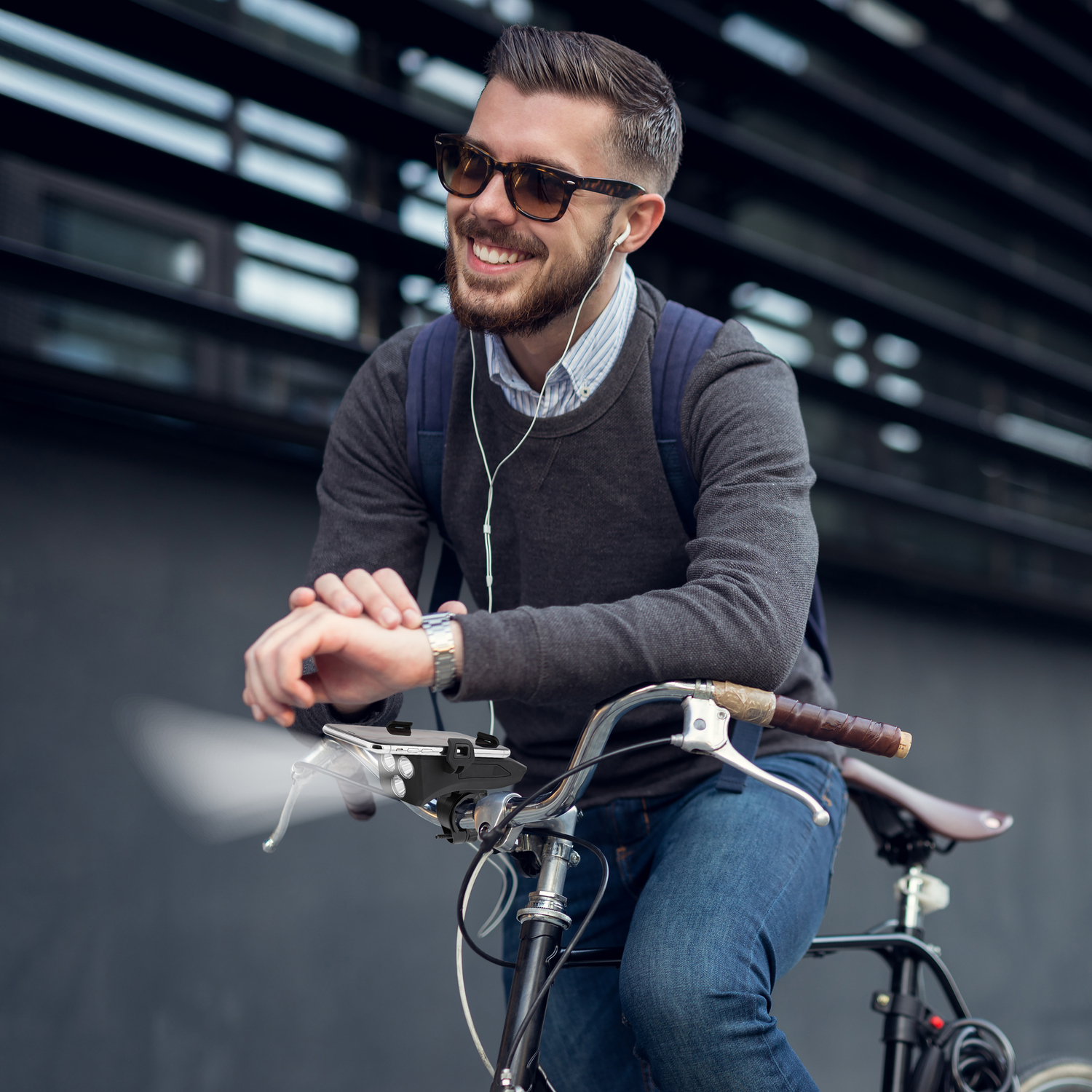 Un homme en lunettes de soleil sourit en s'appuyant sur un vélo. Il porte des écouteurs et un sac à dos.