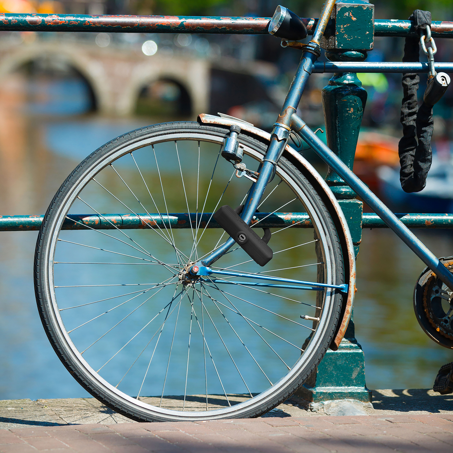 Bicyclette bleue attachée à une rambarde verte. Une rivière et un pont en arrière-plan.