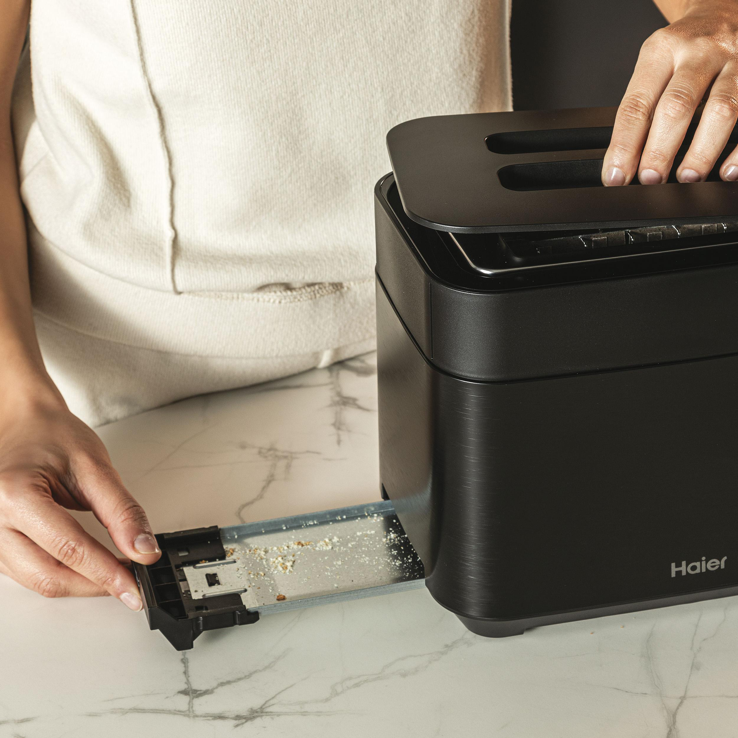 Ein schwarzer Toaster mit herausgezogenem Fach und sichtbaren Händen. Weiße Arbeitsplatte.