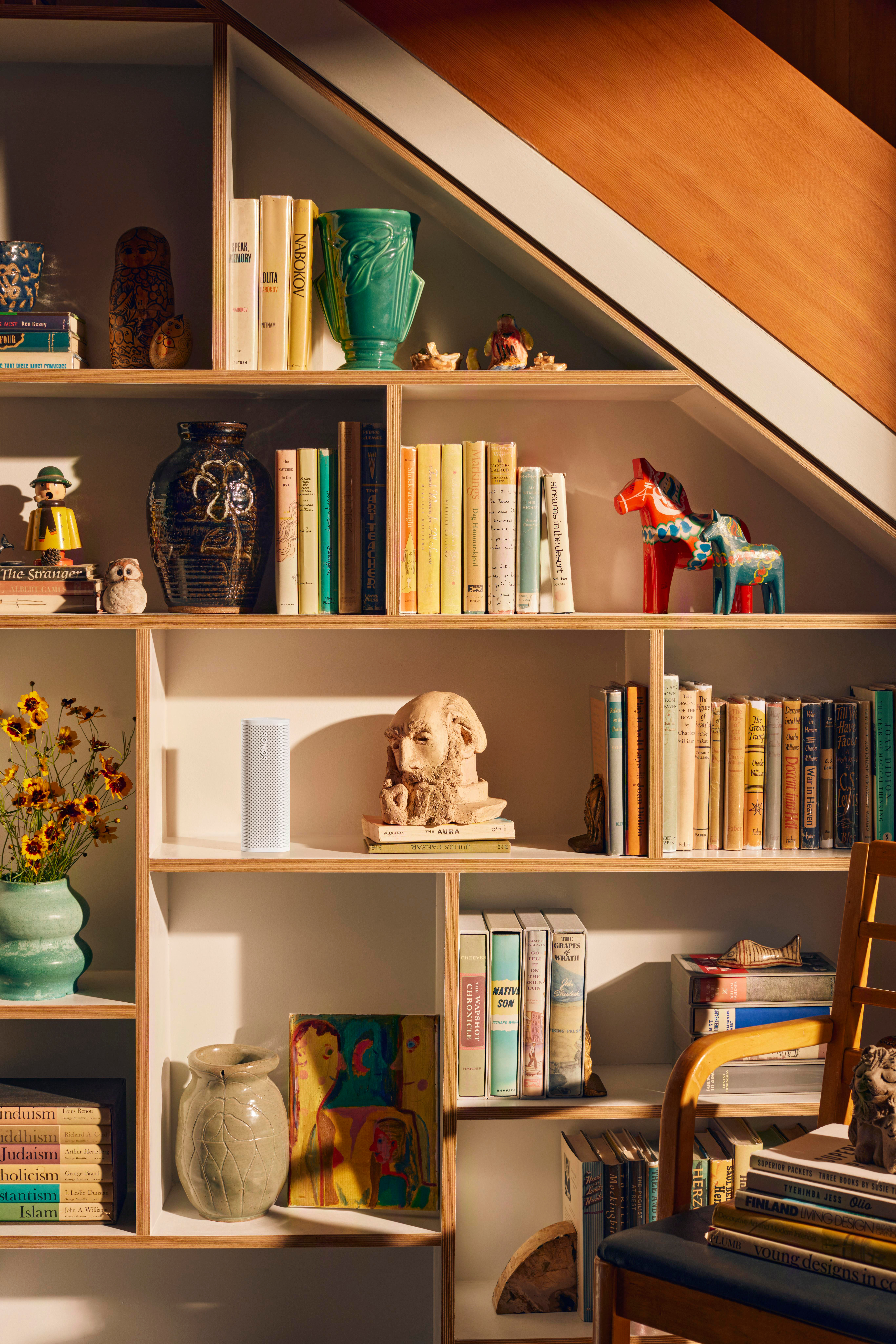 Regale mit Büchern, Vasen und Dekorationen. Eine Holztreppe ist im Hintergrund sichtbar.
