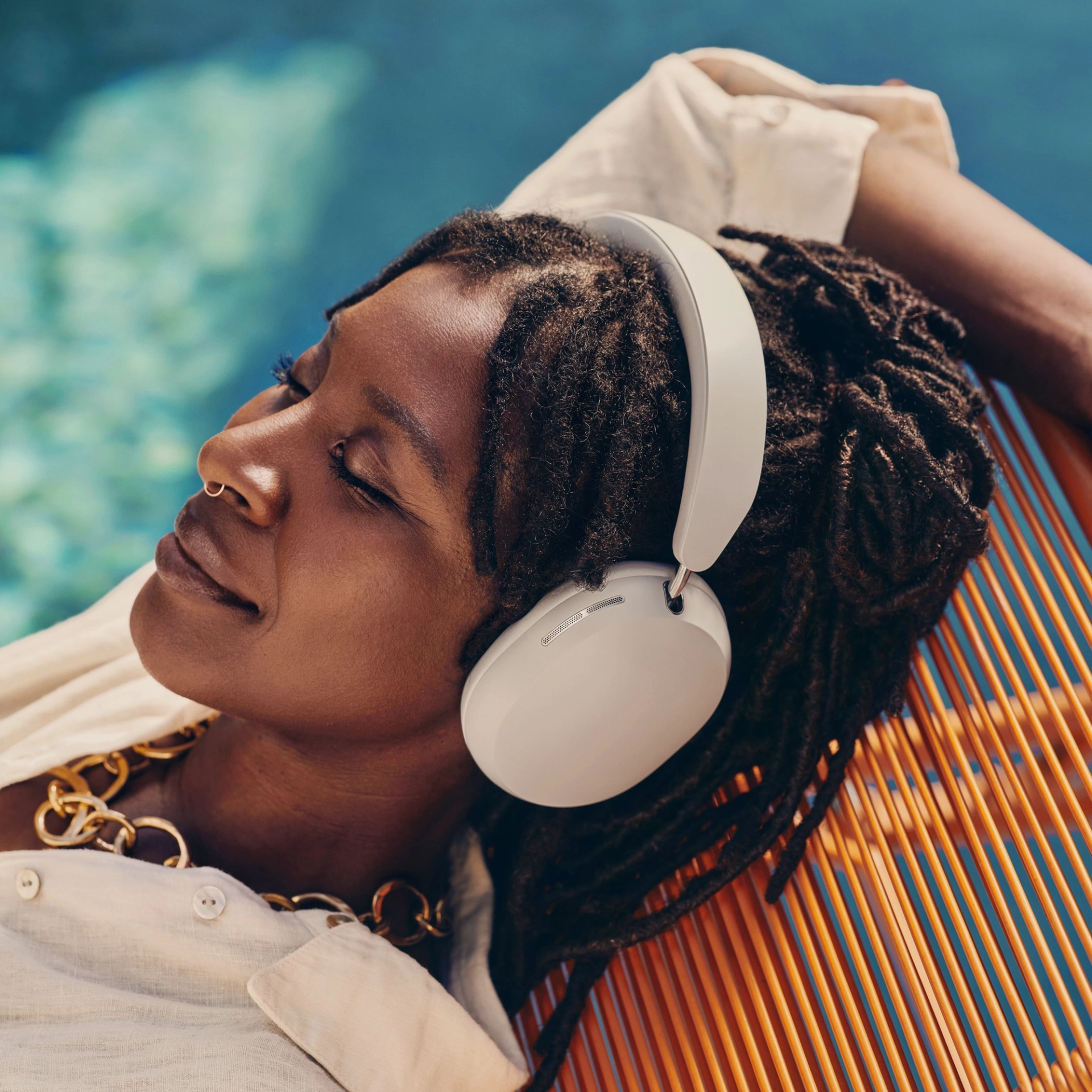 Une personne avec un casque gris, se relaxant au bord d'une piscine sur une chaise orange.