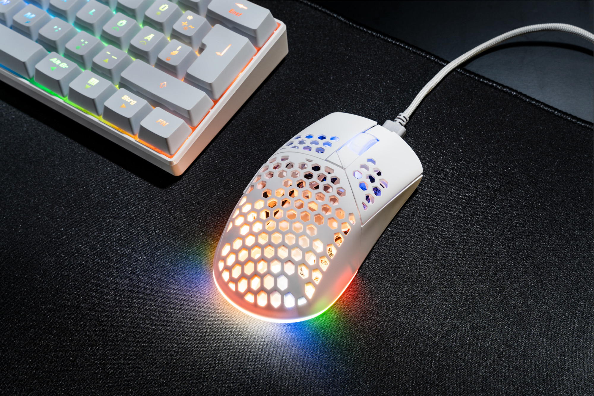 Biała mysz do gier i klawiatura na czarnej podkładce. Światła są włączone.