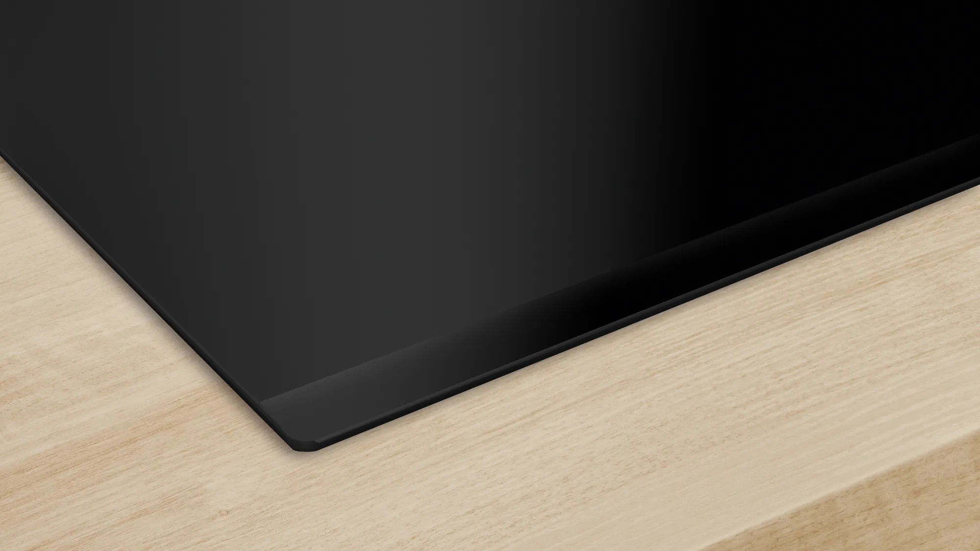 Czarna płyta kuchenna na jasnej drewnianej powierzchni. Krawędź jest czarna i występuje ciemna obwódka.