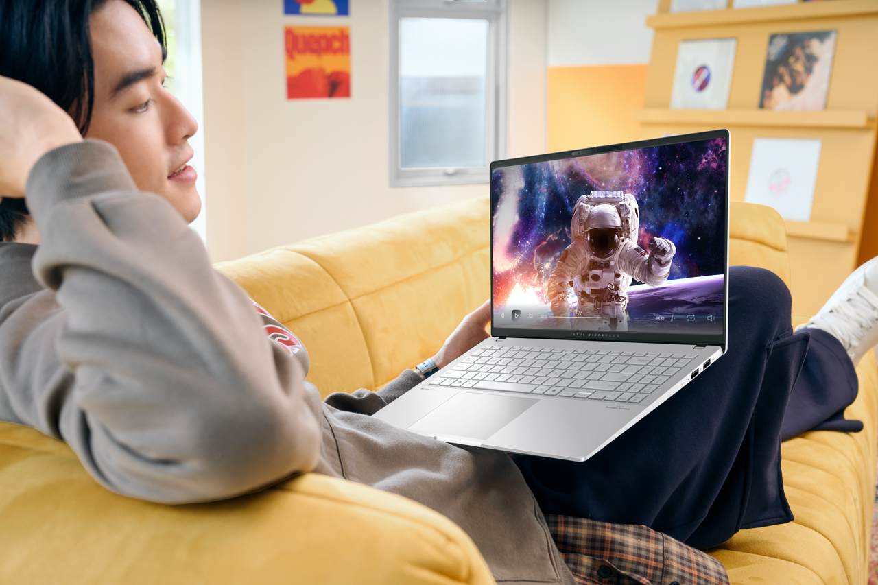 Mann sieht Laptop mit Astronaut auf dem Bildschirm, sitzt auf gelbem Sofa.