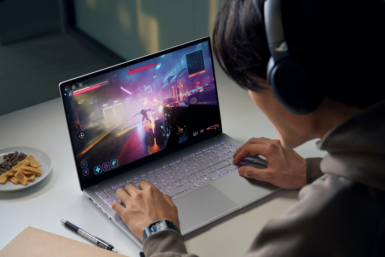 Person spielt Videospiel auf einem Laptop. Tastatur leuchtet. Snacks auf dem Tisch.