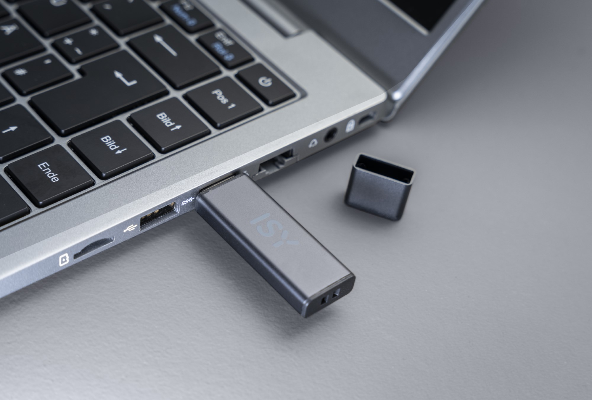 Pendrive włożony do laptopa. Szary metaliczny pendrive i laptop ze srebrnym wykończeniem.