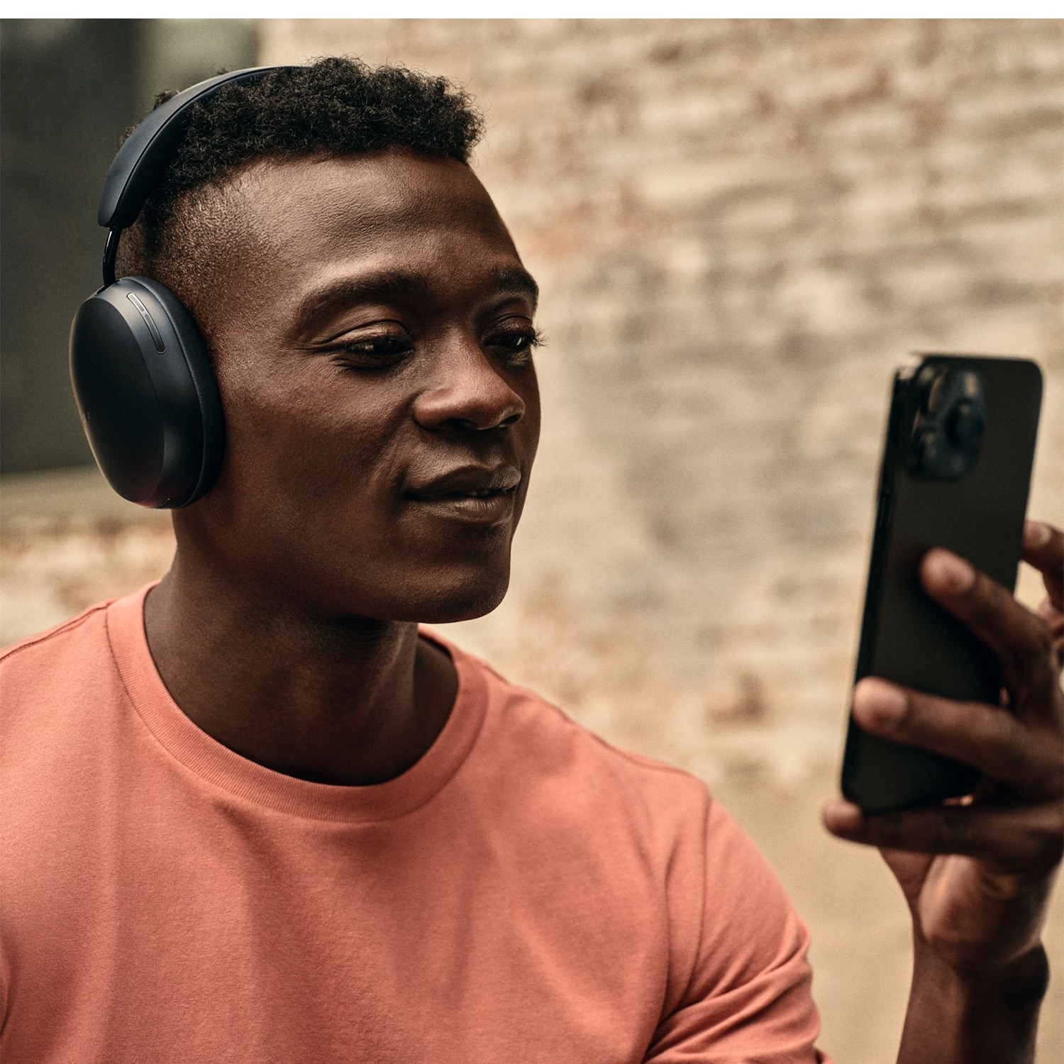 Un uomo nero con le cuffie, che tiene un telefono, guardandolo.
