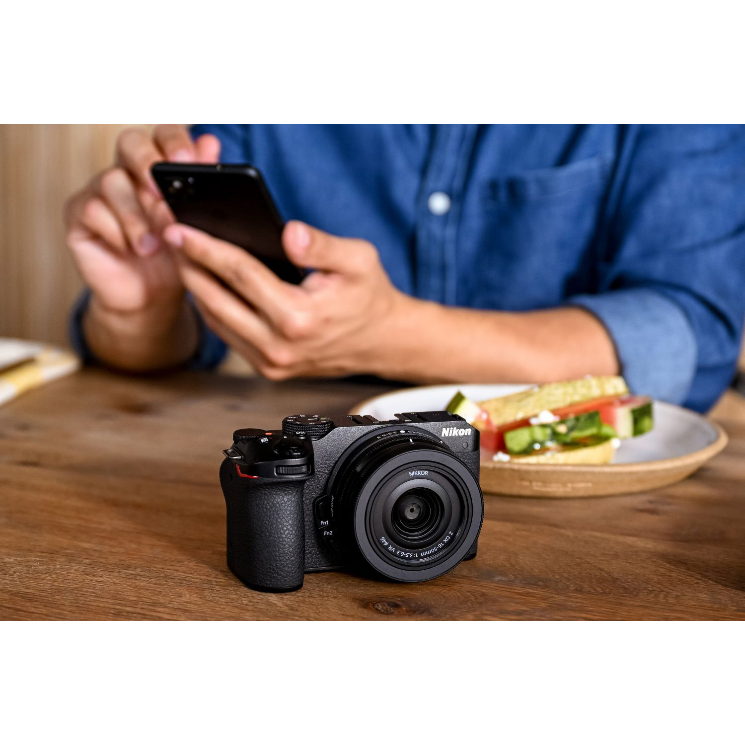 Persona che tiene un telefono, con fotocamera e cibo sul tavolo.
