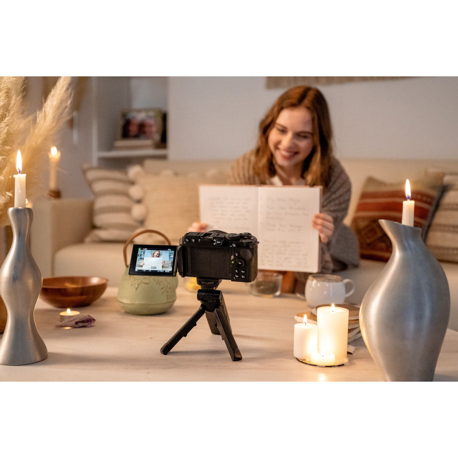 Una donna che filma con una fotocamera su un treppiede, candele e decorazioni su un tavolo in un ambiente domestico.