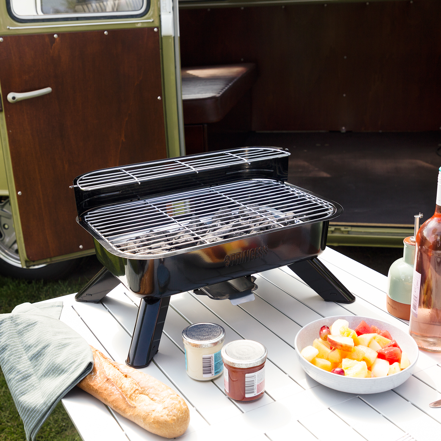 Un grill nero su un tavolo con cibo e un furgone sullo sfondo.
